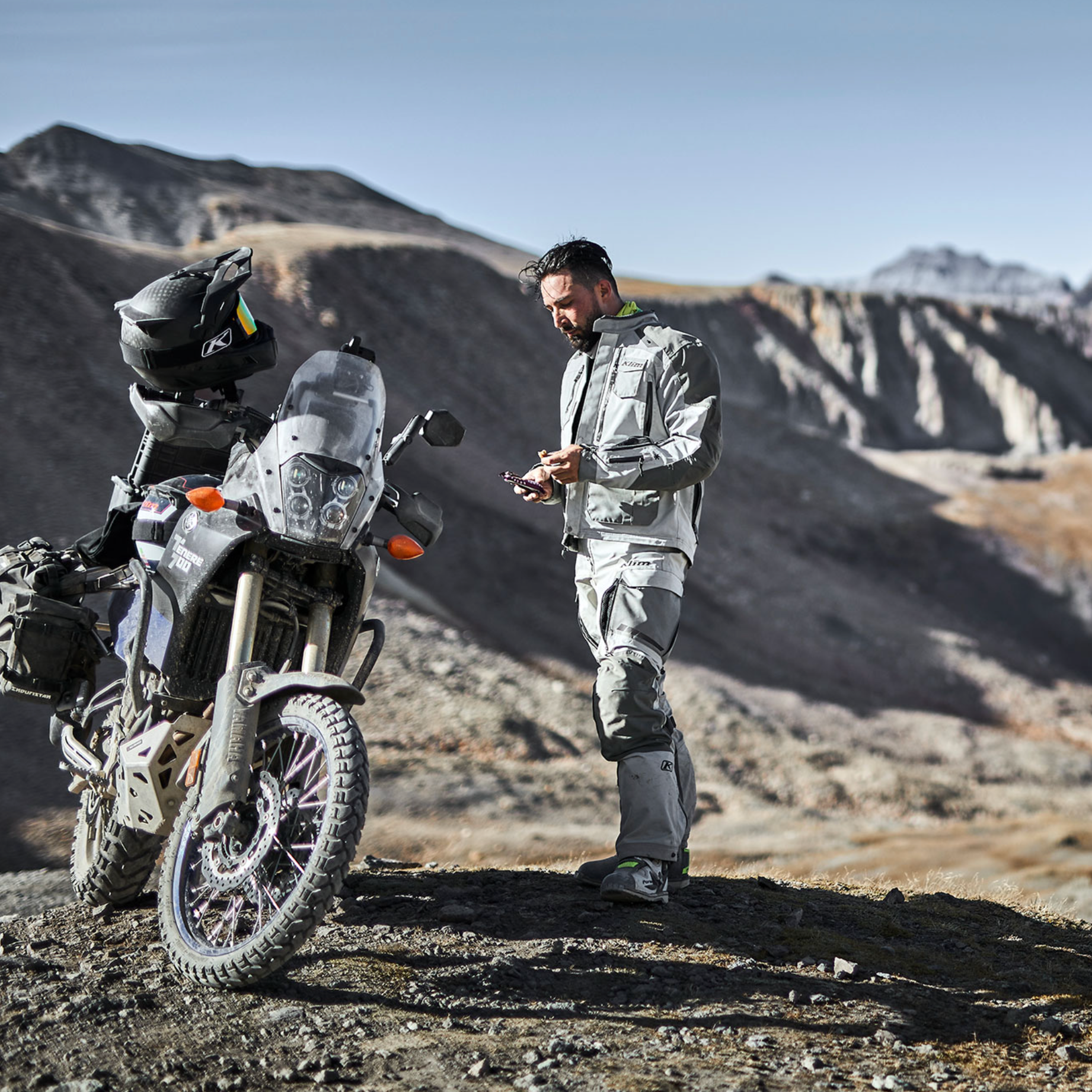 Man standing next to a motorcycle in a desert landscape with mountains in the background, text 'LONG DISTANCE COMFORT' at the bottom.