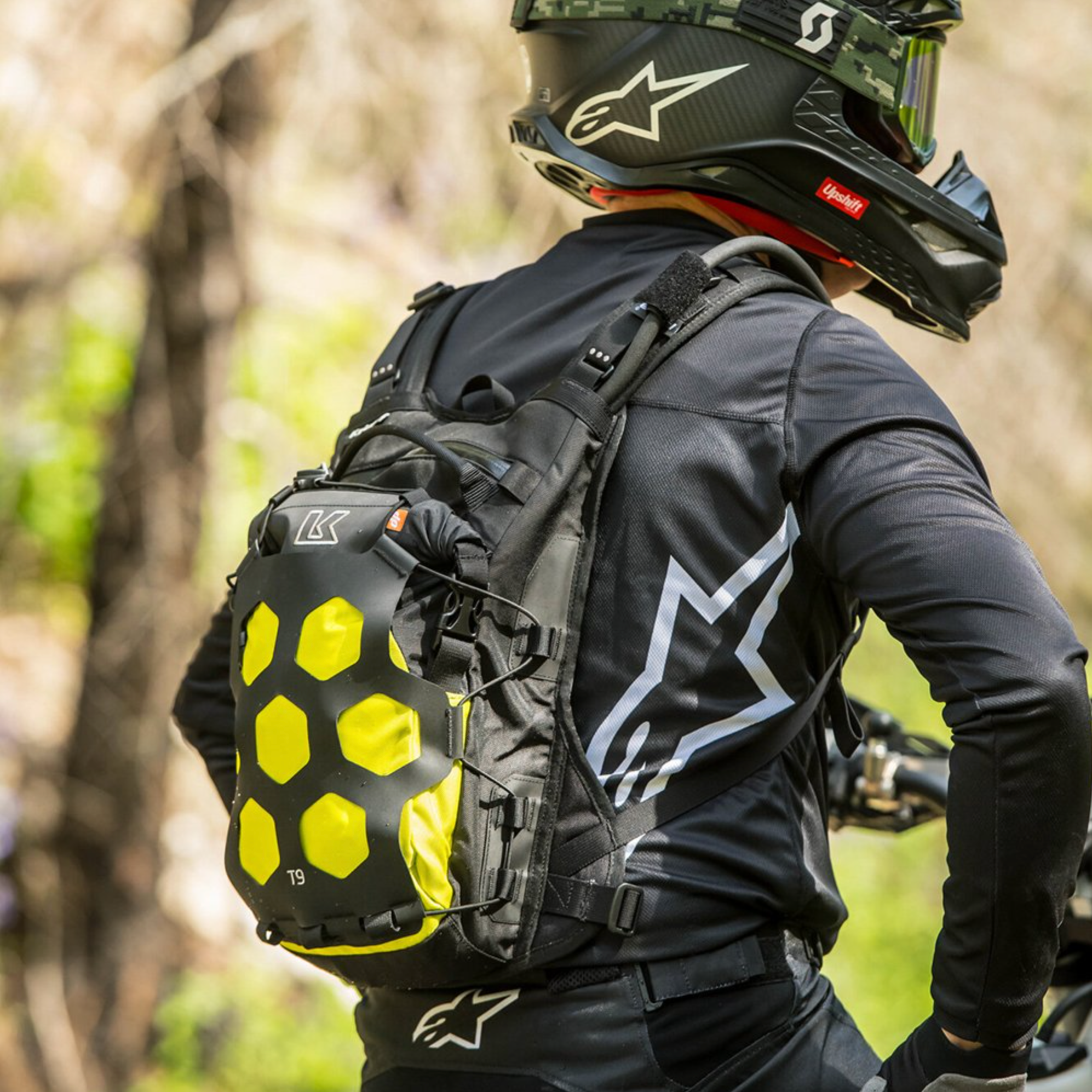 Person wearing a black helmet and backpack with a forest background