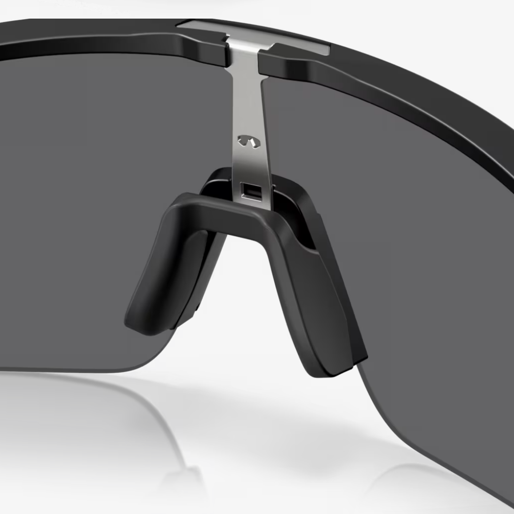 Close-up of a shield-style sunglasses lens and frame in black with a dark gray lens and a small silver metal accent at the top.