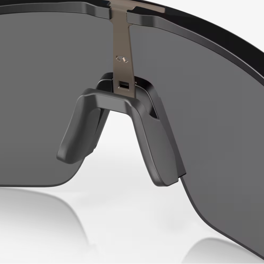 Close-up of a black wraparound shield-style sunglasses lens and nose bridge on a light gray background.