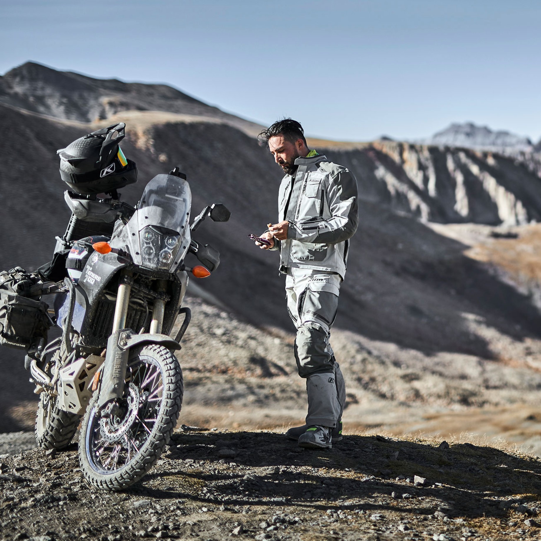 Man standing next to a motorcycle in a desert landscape with mountains in the background, text 'LONG DISTANCE COMFORT' at the bottom.