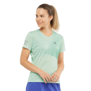 Woman wearing a light green athletic shirt with a brand logo on a white background