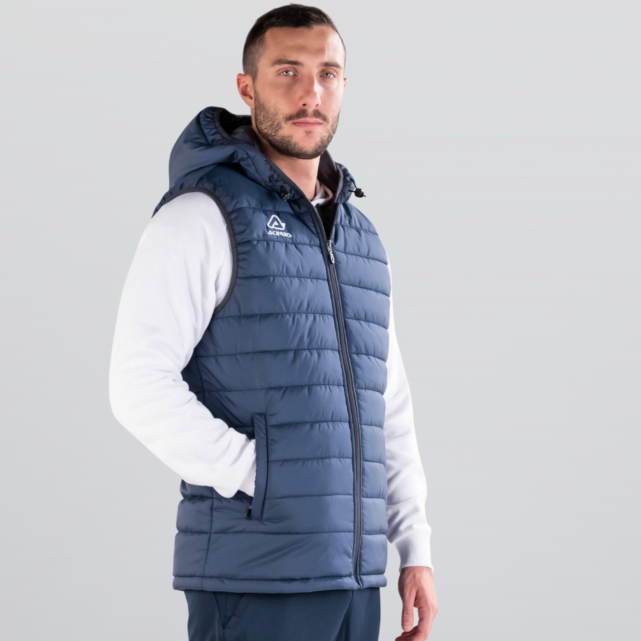 Man wearing a blue puffer vest over a white shirt with navy pants on a gray background