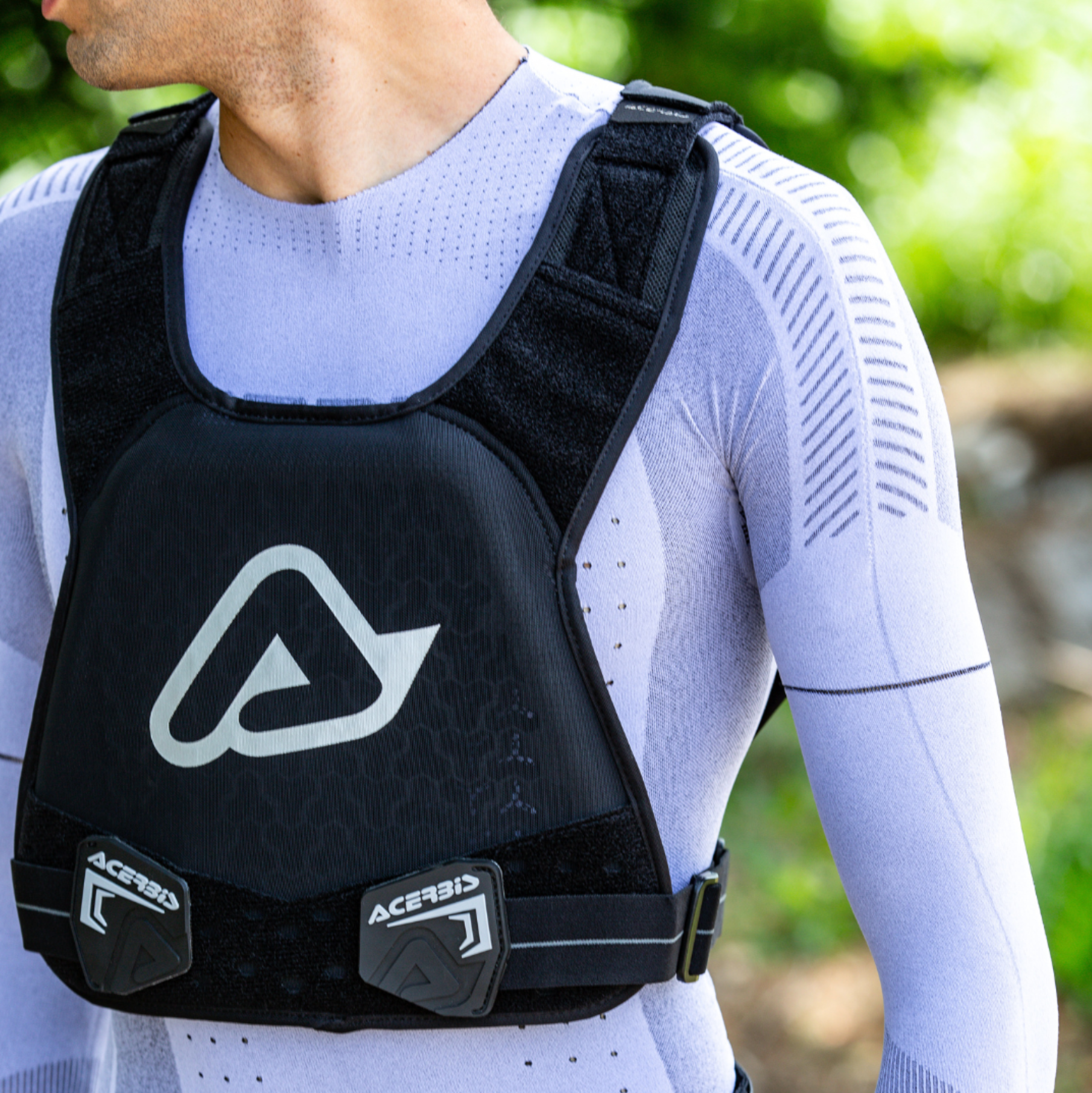 Person wearing a black Acerbis chest protector with a blurred green background
