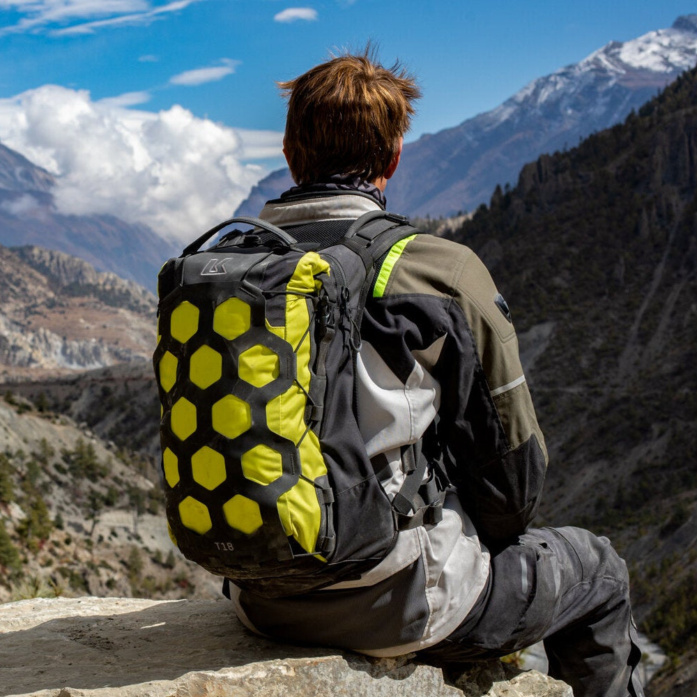 Person with a backpack sitting on a rock overlooking a mountainous landscape.